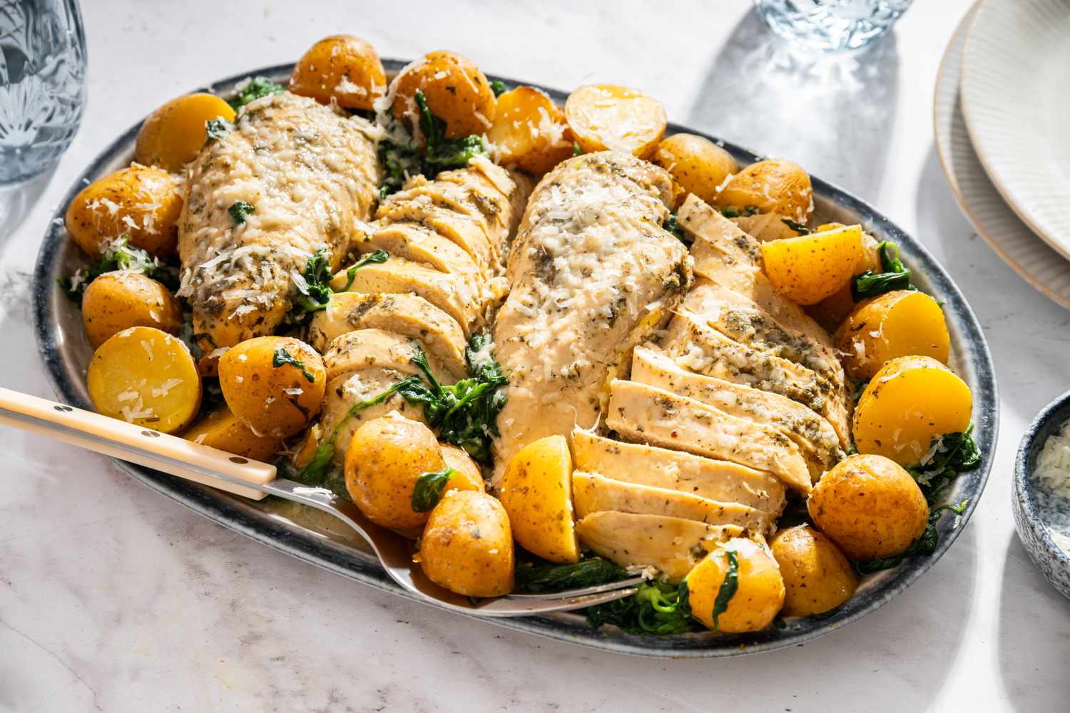 A platter with cooked chicken breast slices and whole small potatoes garnished with herbs