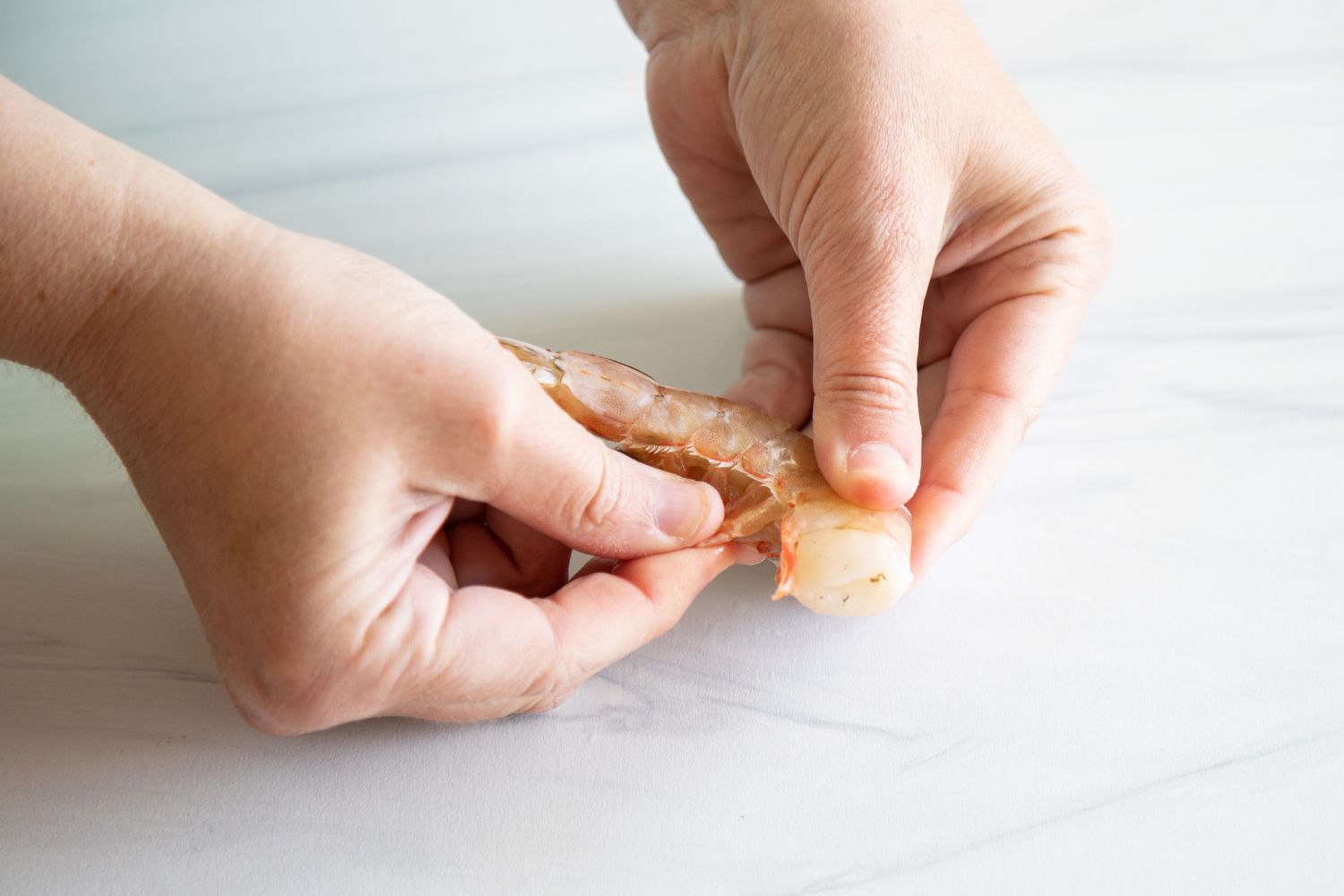 Hands showing how to devein shrimp.