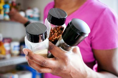A person holding three spice jars in their hand standing near a pantry