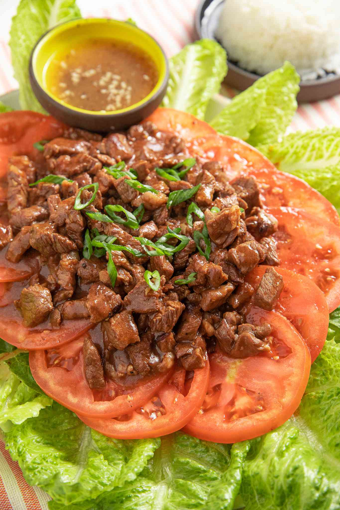 Lok Lak Served Over Sliced Tomatoes and Lettuce on a Platter With a Bowl of Pepper-Lime Sauce, and in the Background, a Bowl of Rice