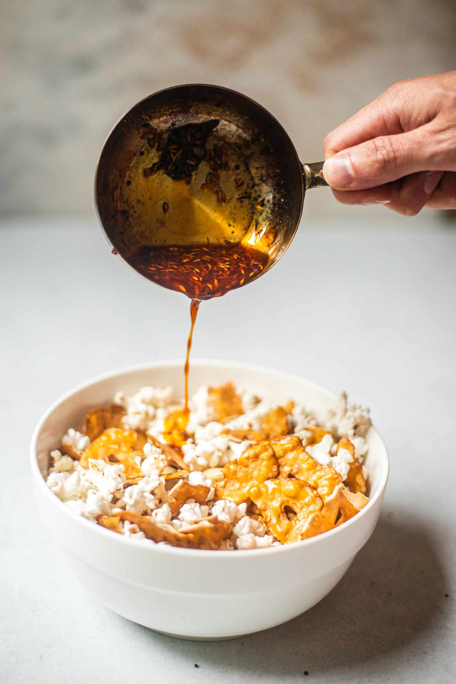 Pouring bloomed spice mixture over a snack bowl