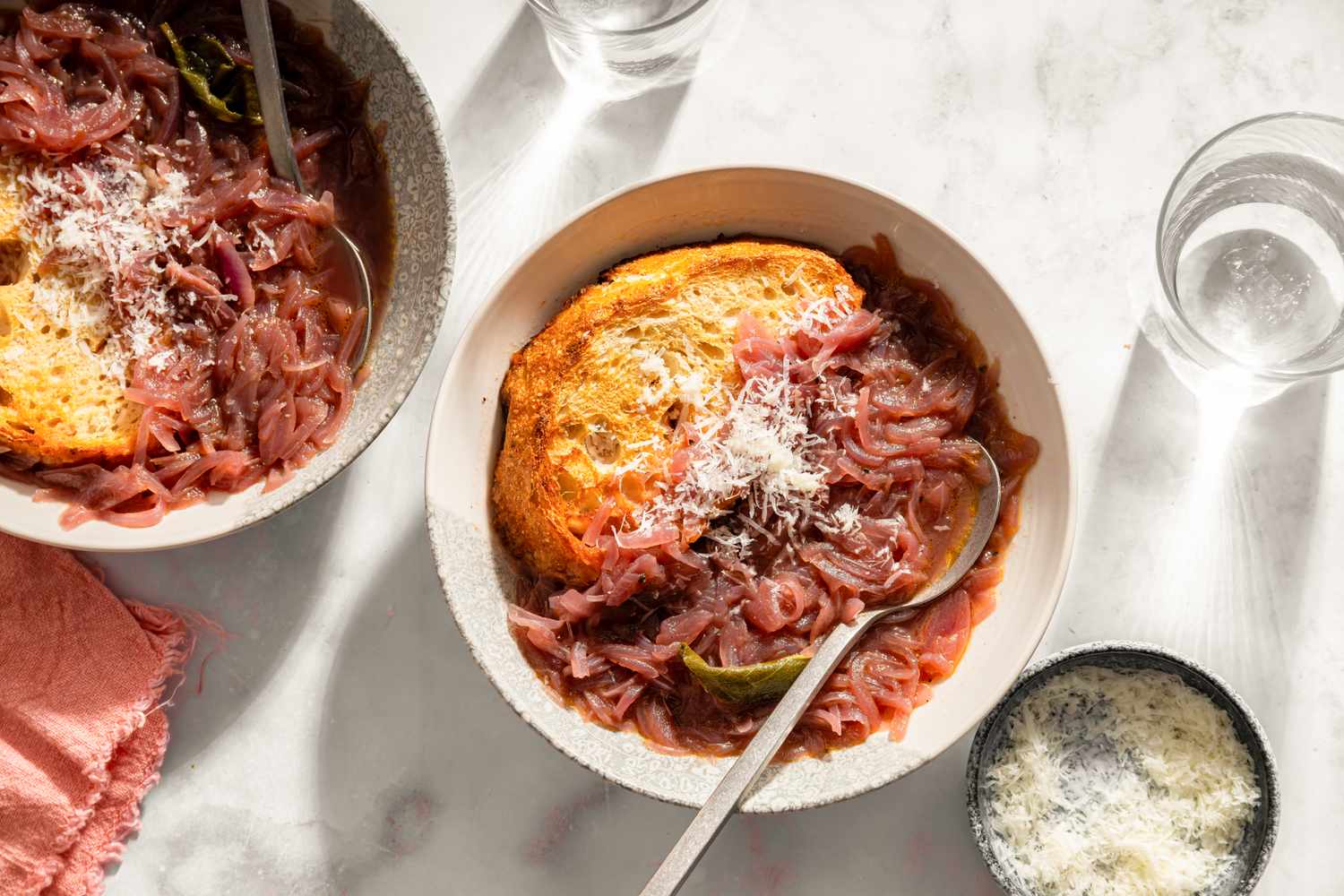 Bowls of Tuscan onion soup with bread and grated cheese on a light surface