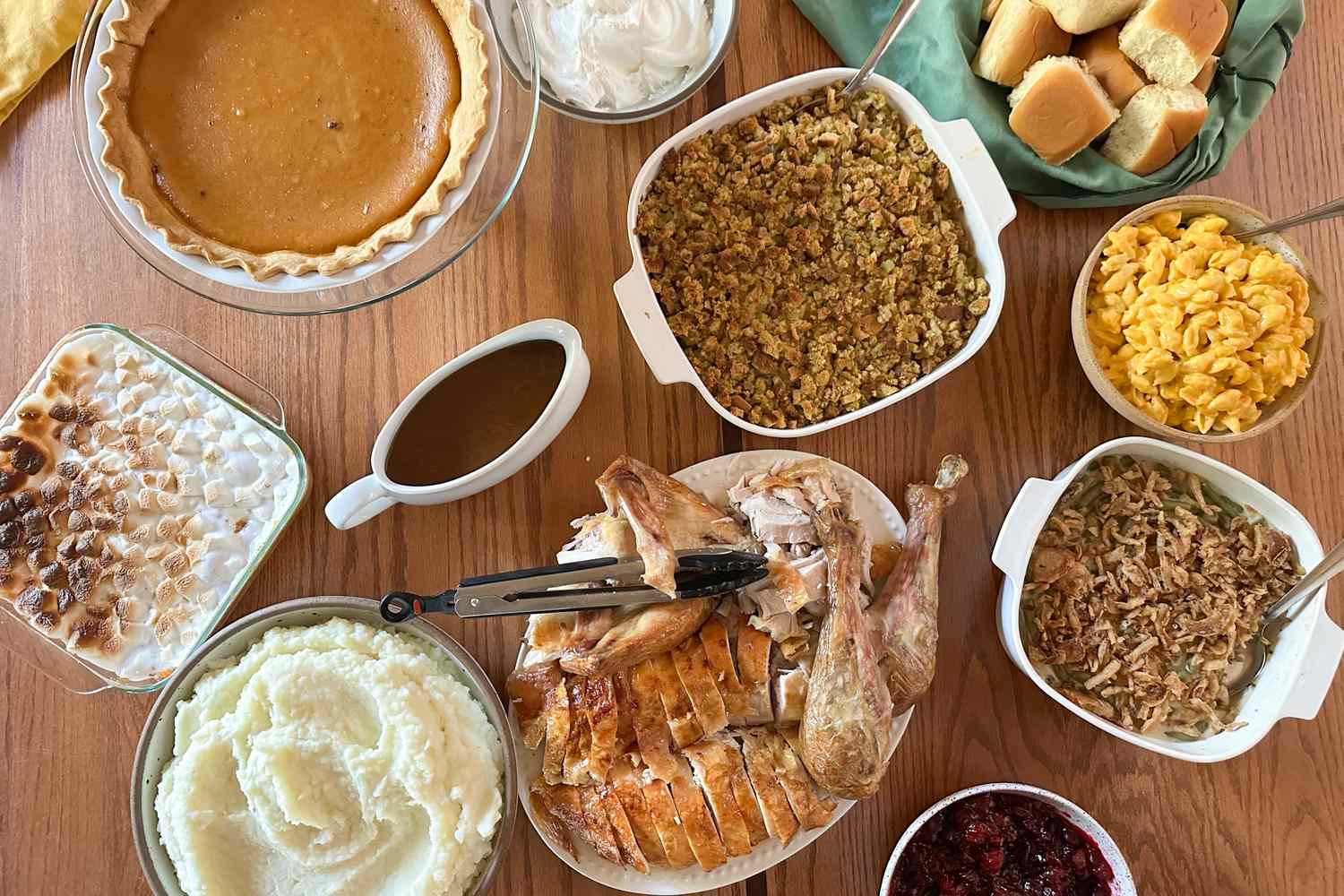 A Thanksgiving meal spread including turkey mashed potatoes rolls pie and various side dishes set on a table