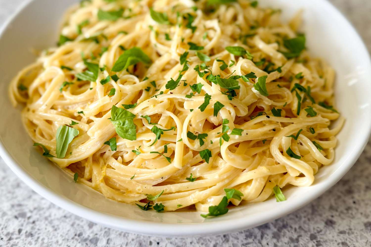 Lemon linguine garnished with parsley and basil served in a bowl.