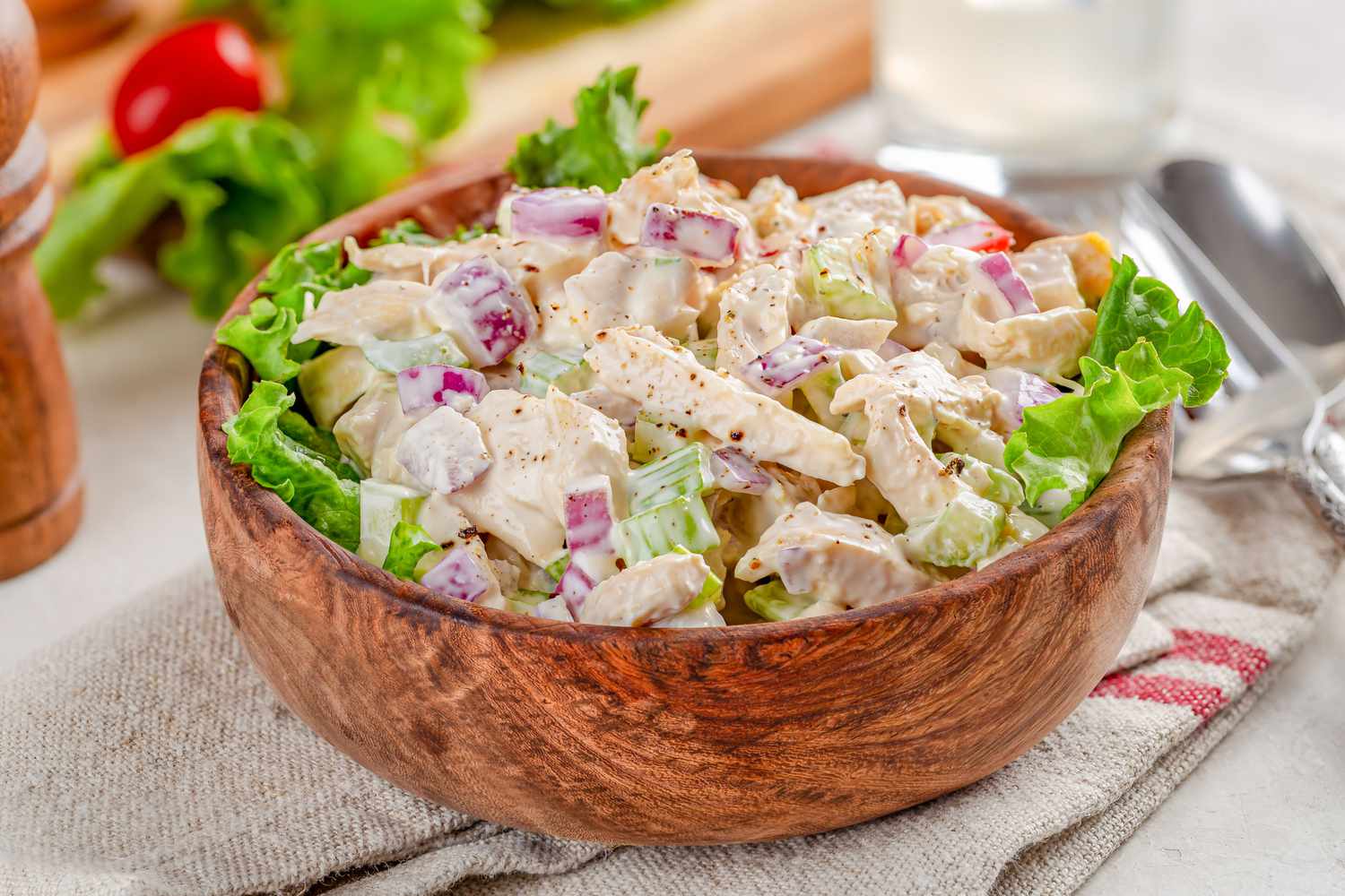 Chicken salad with lettuce and grape tomatoes in a wooden bowl on a napkin