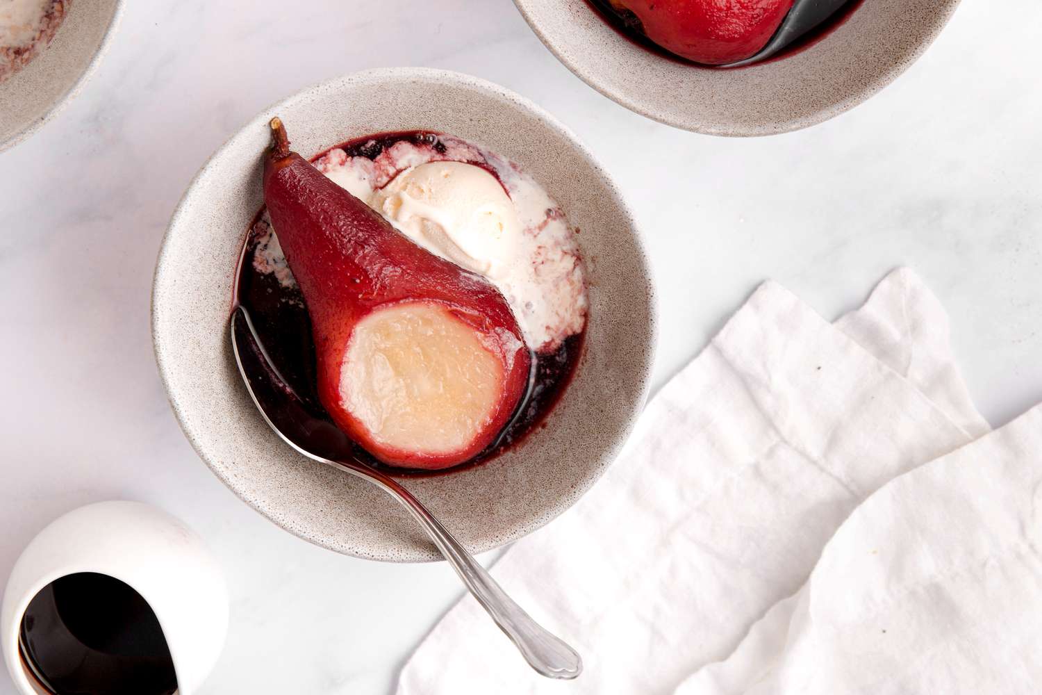 Poached pear in small white bowl with ice cream.