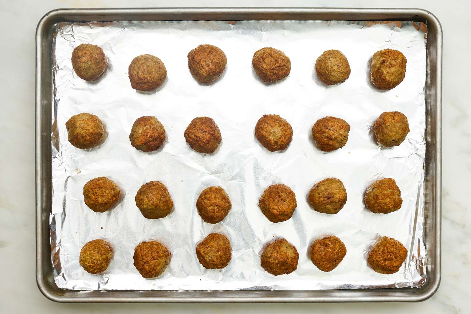Baked store-bought meatballs on an aluminium foil lined baking tray