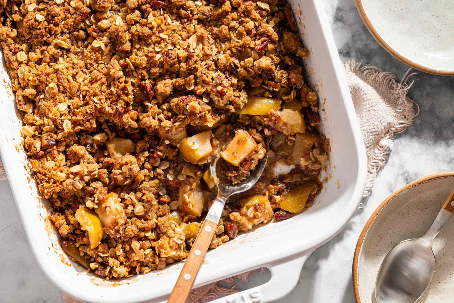 A baked apple crisp in a white rectangular dish with a serving spoon