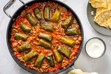 A skillet with dolmas cooked in tomato sauce and ground beef, served with pita bread and yogurt