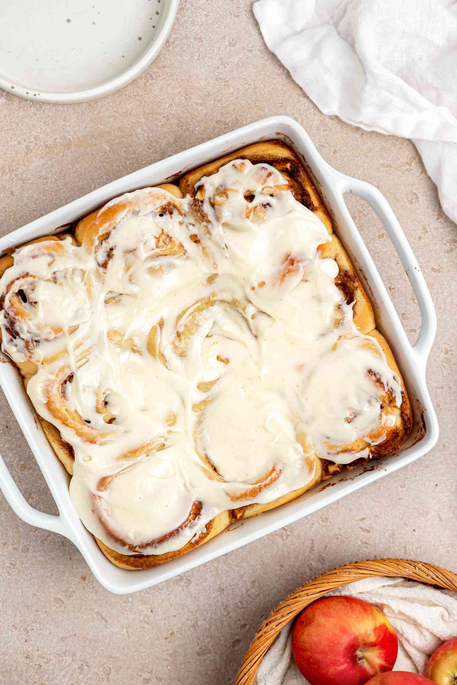 Apple Cinnamon Rolls with Cream Cheese Frosting Next to a Bowl of Apples