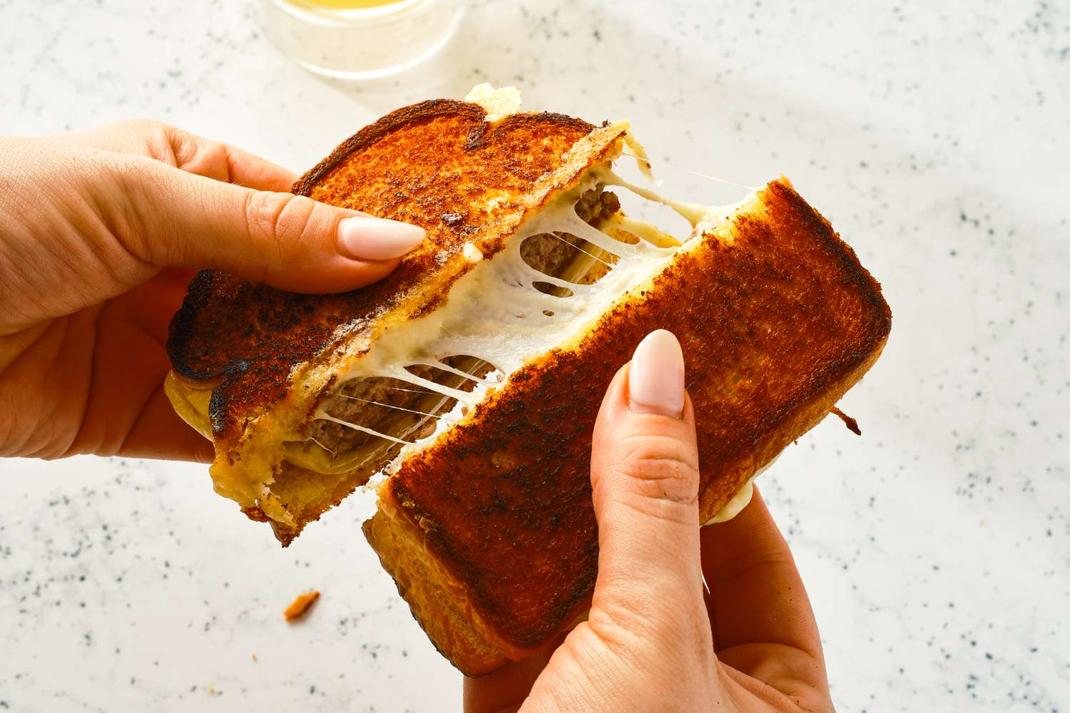 A close-up of hands pulling apart a cheesy patty melt sandwich