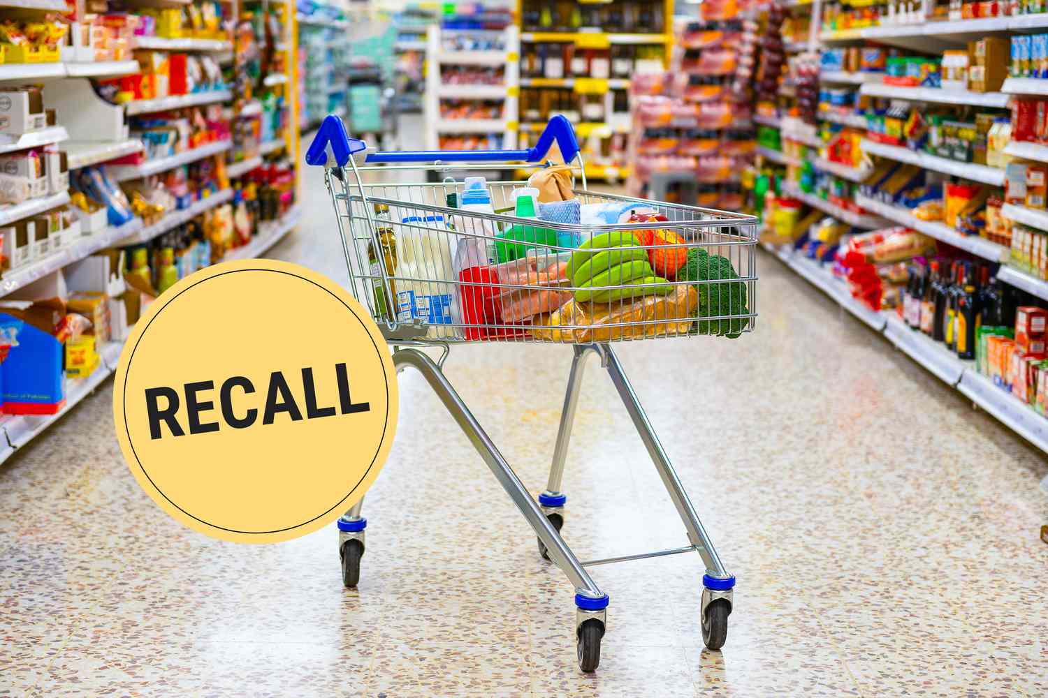 Looking down a grocery store aisle. A shopping cart filled with bananas, milk, and other grocery basics is in the middle of the aisle.