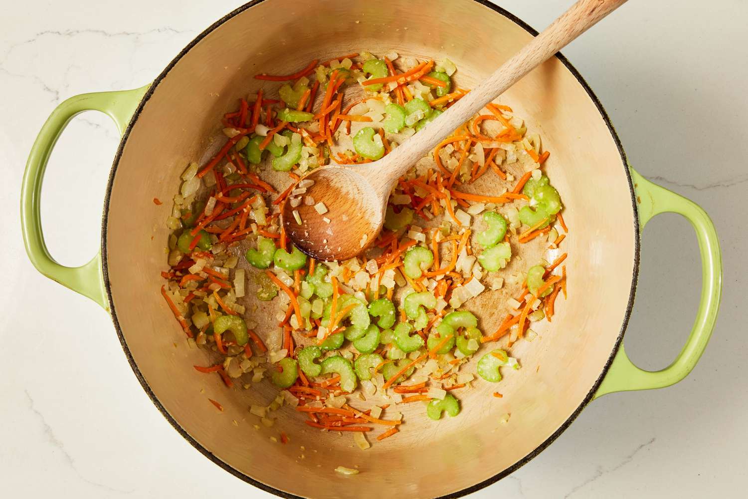 Vegetables sauteed in a Dutch oven and mixed using a wooden spoon for copycat Olive Garden chicken and gnocchi soup recipe
