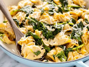 Close Up of Skillet Cacio e Pepe Tortellini With Wilted Greens in a Pot With a Wooden Serving Spoon