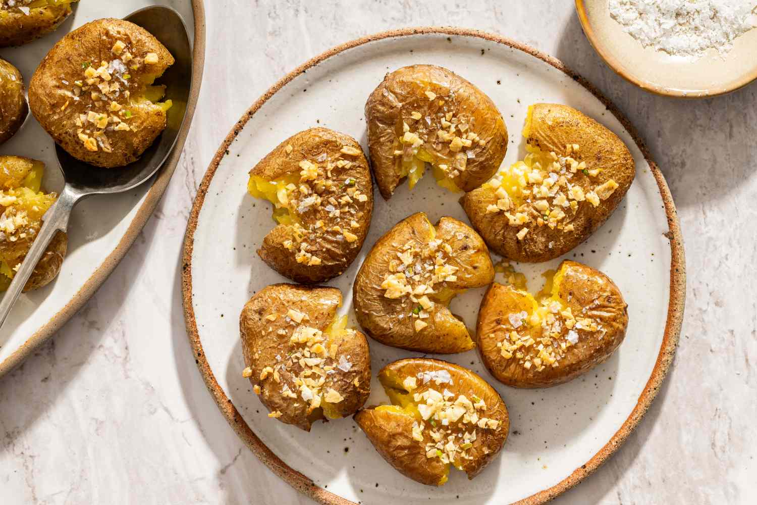 Rustic smashed potatoes served on a plate garnished with crumbs and surrounded by side dishes or condiments