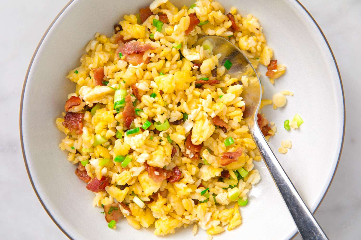 Bowl of fried rice with egg, bacon, and green onions, spoon included