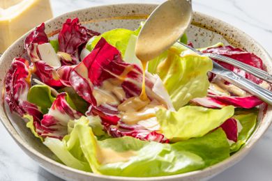 A bowl of salad with lettuce and radicchio leaves, a spoon is drizzling vinaigrette over the salad