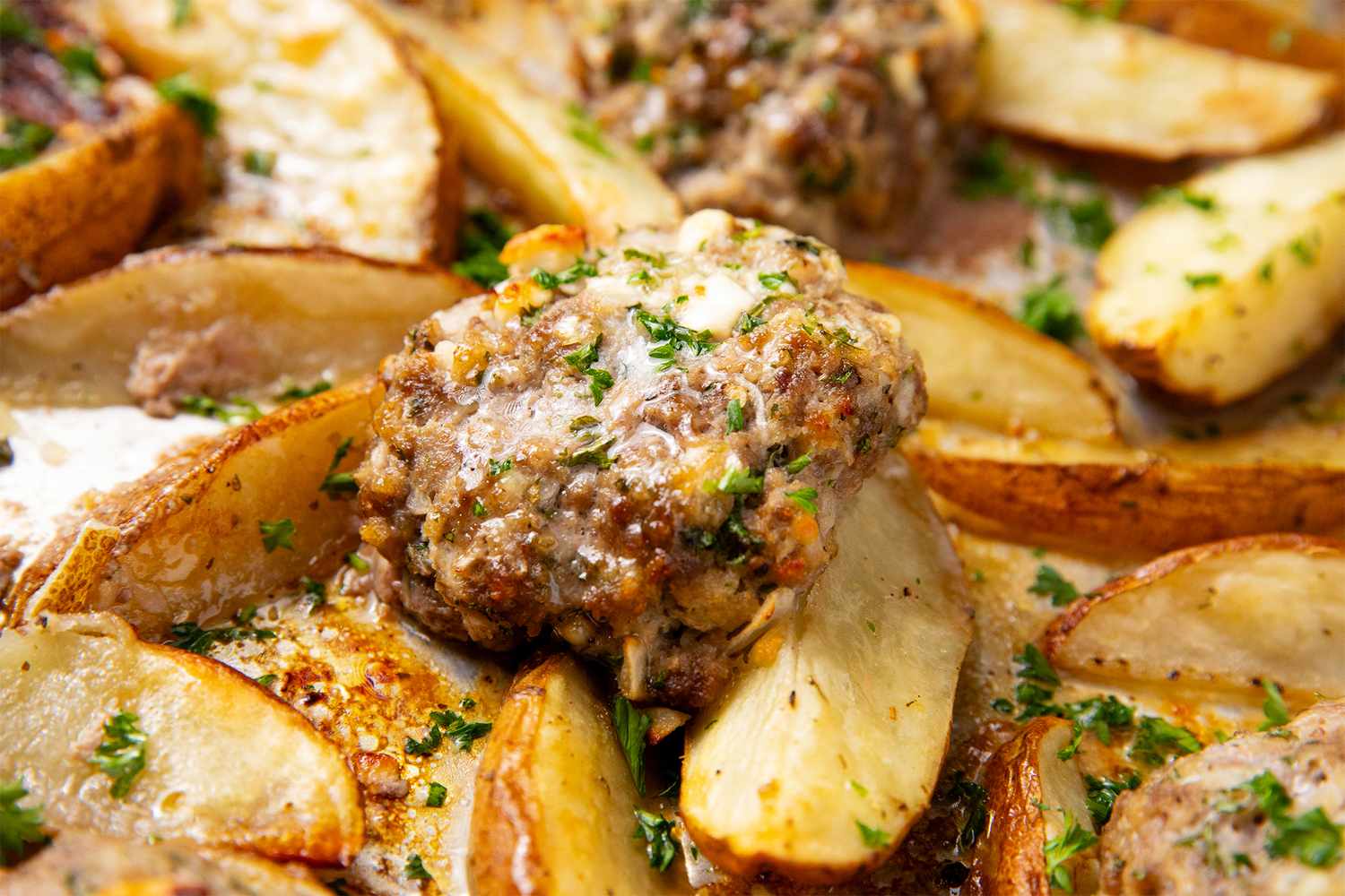 Baked meat patties with seasoned potato wedges and parsley garnish on a tray