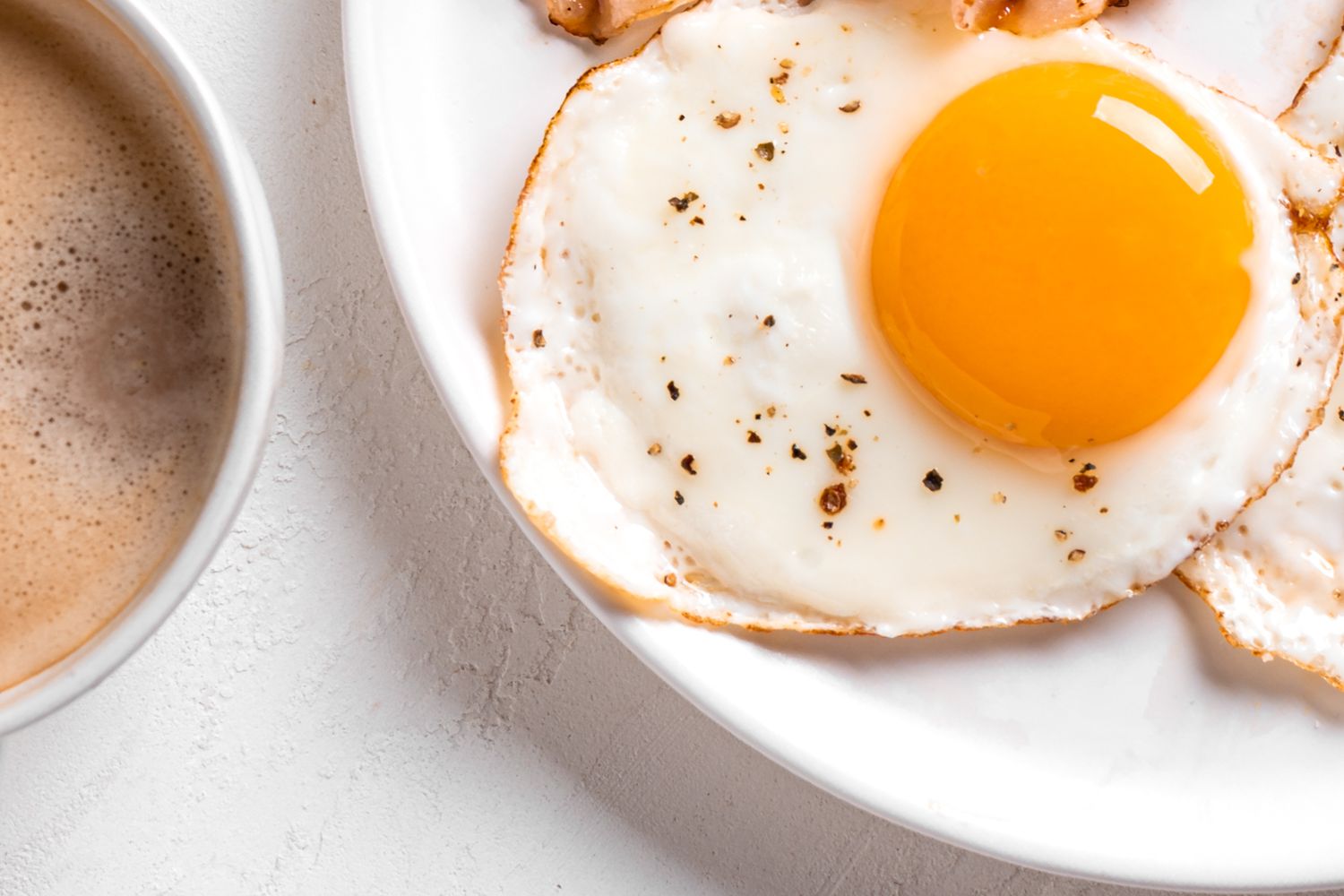 Close up of a sunny side up egg on a plate with a mug of coffee peeking in