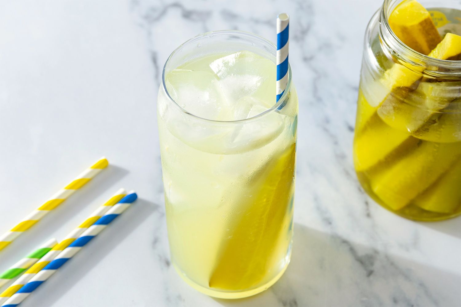 Pickle Lemonade in a glass with a straw, jar of pickle spears, extra straws