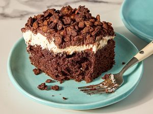 A slice of chocolate cake with cream topping and chocolate pieces on a plate with a fork