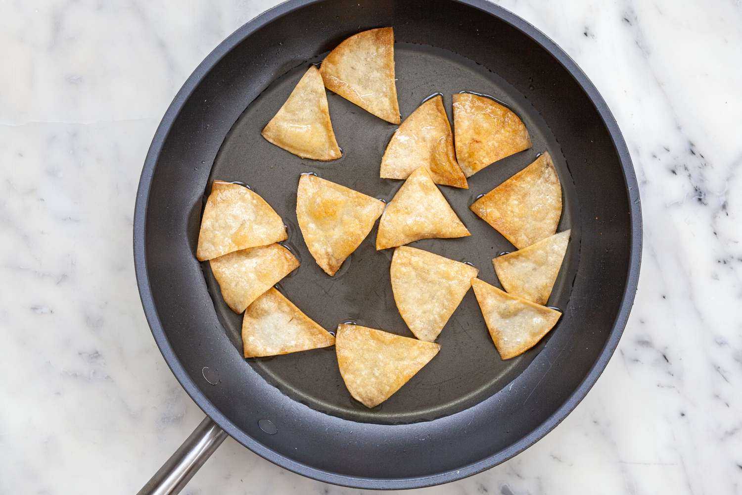 Tortilla chips frying in a skillet to make Chilaquiles.