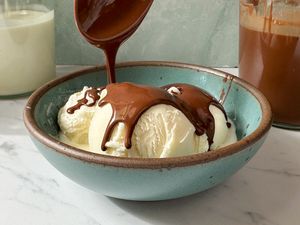 Vanilla ice cream in a bowl being topped with melted chocolate sauce