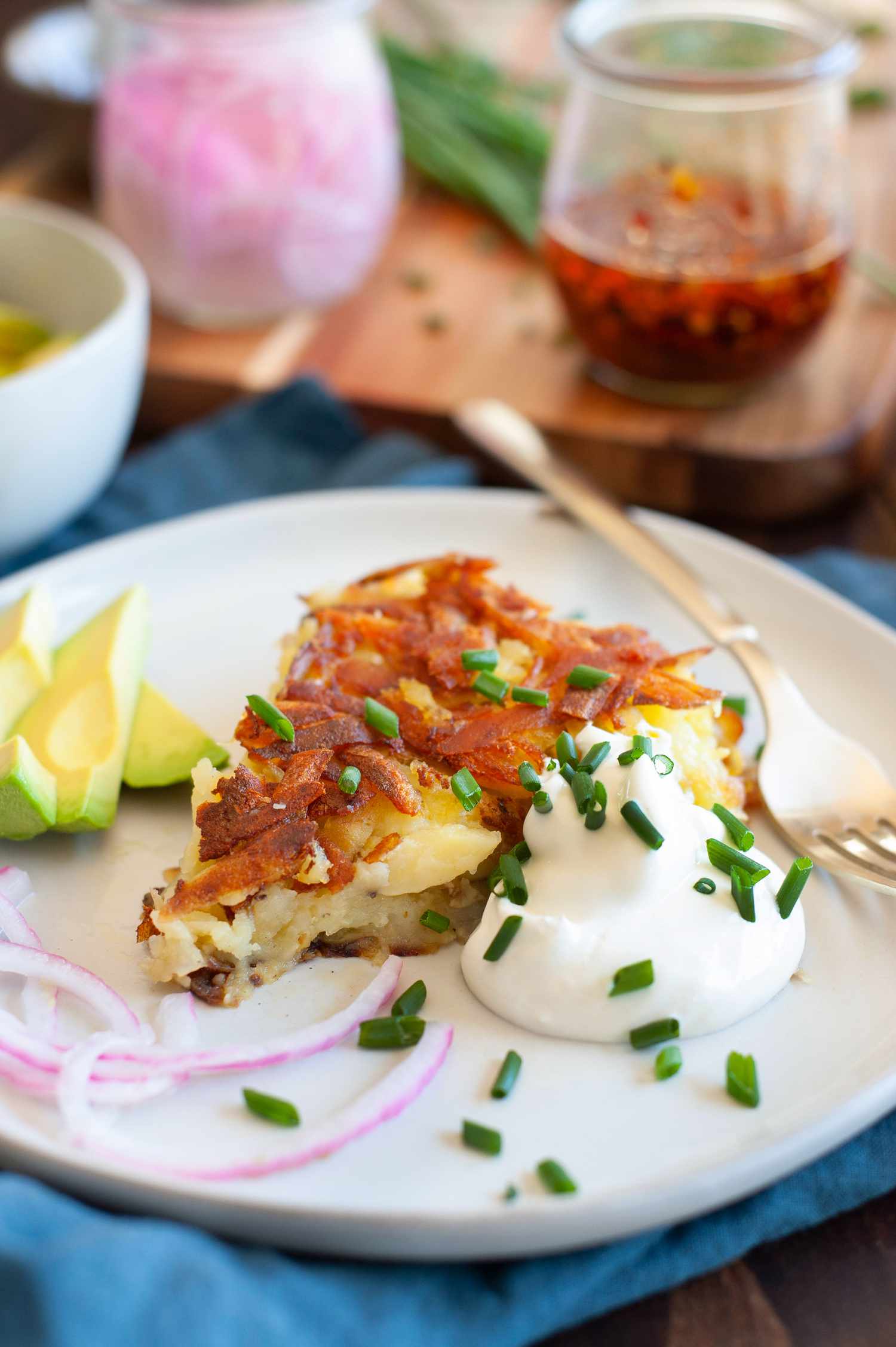 Slice of Rosti on a Plate with Sour Cream, Sliced Avocados, and Sliced Onions