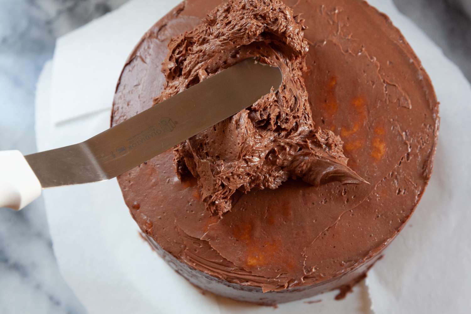 Overhead view showing how to frost a layer cake with chocolate frosting.
