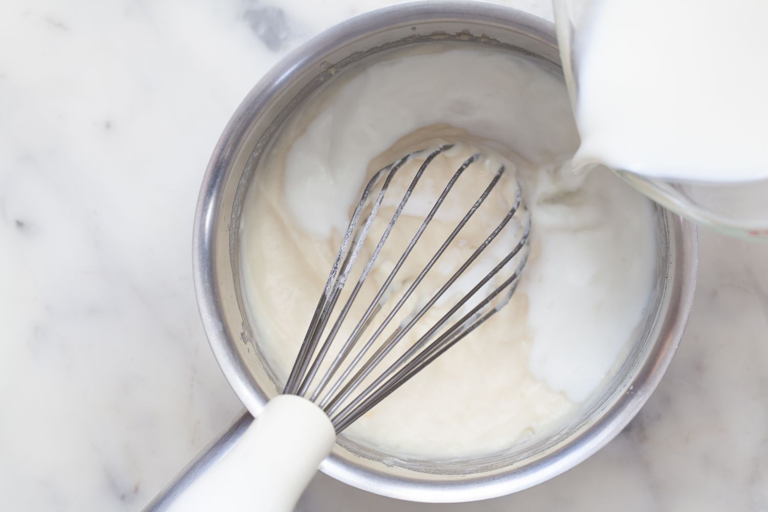 Adding milk to a saucepan with béchamel sauce (white sauce)