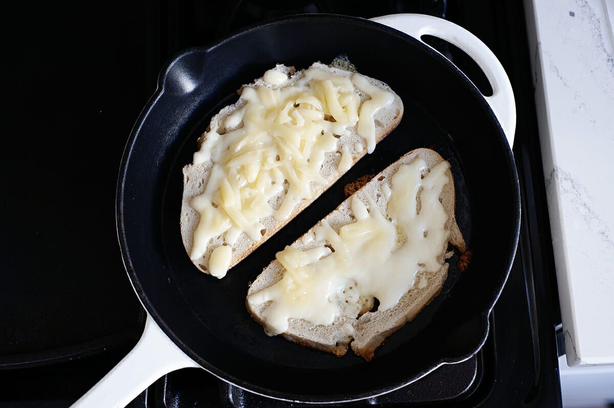 Two slices of bread, set open faced with shredded cheese on top in a cast iron skillet.