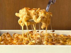 large serving spoon scooping Tini Younger’s Mac and Cheese out of a dish, cheese pull strings hanging