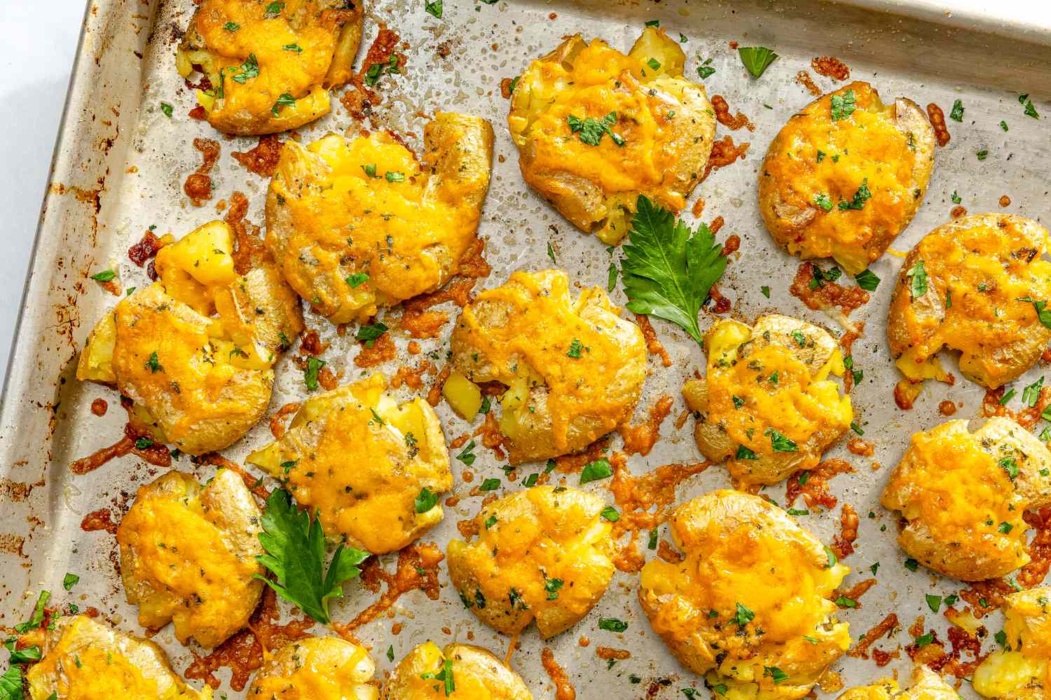 Baked smashed potatoes topped with cheese and herbs on a baking sheet