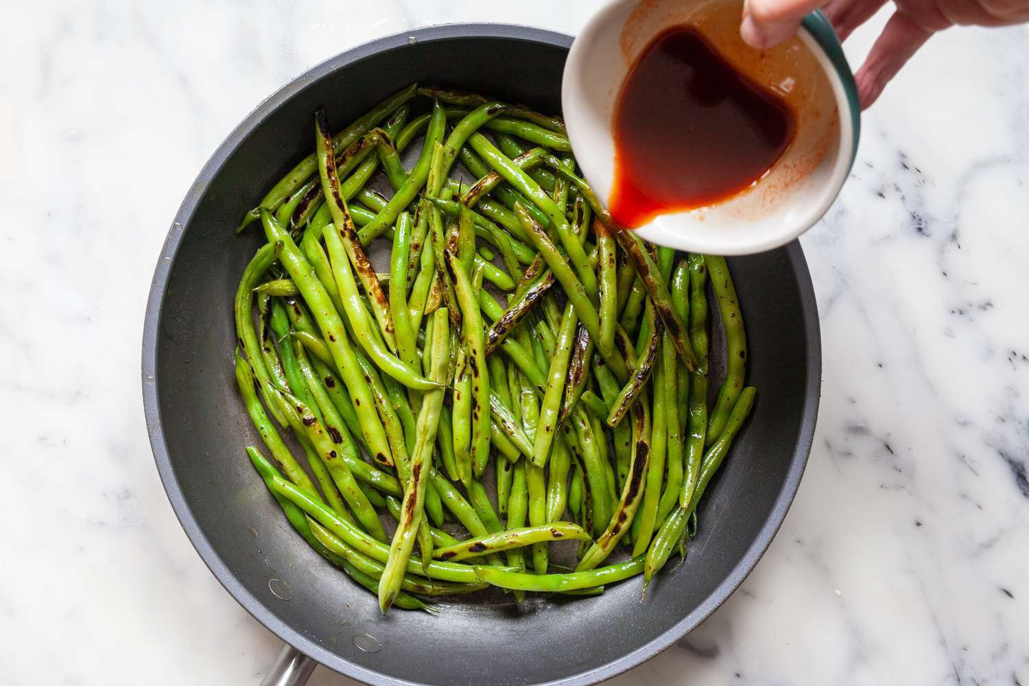 pouring sauce over cooked green beans