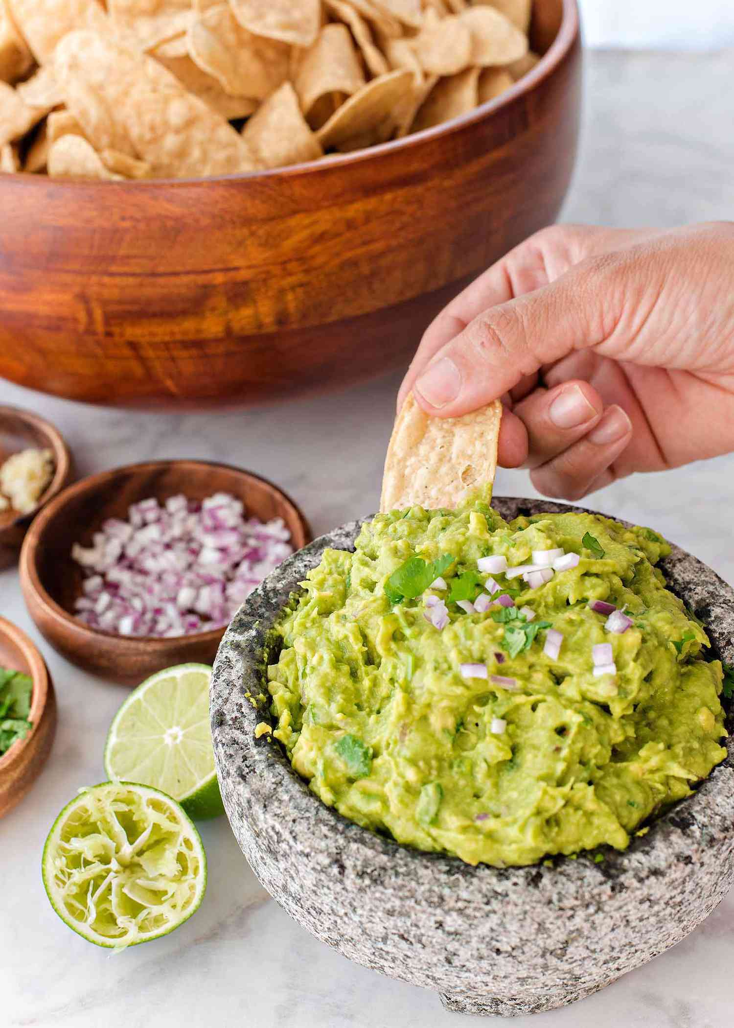 How to Make Guacamole - guacamole in a bowl with someone dipping a chip into it