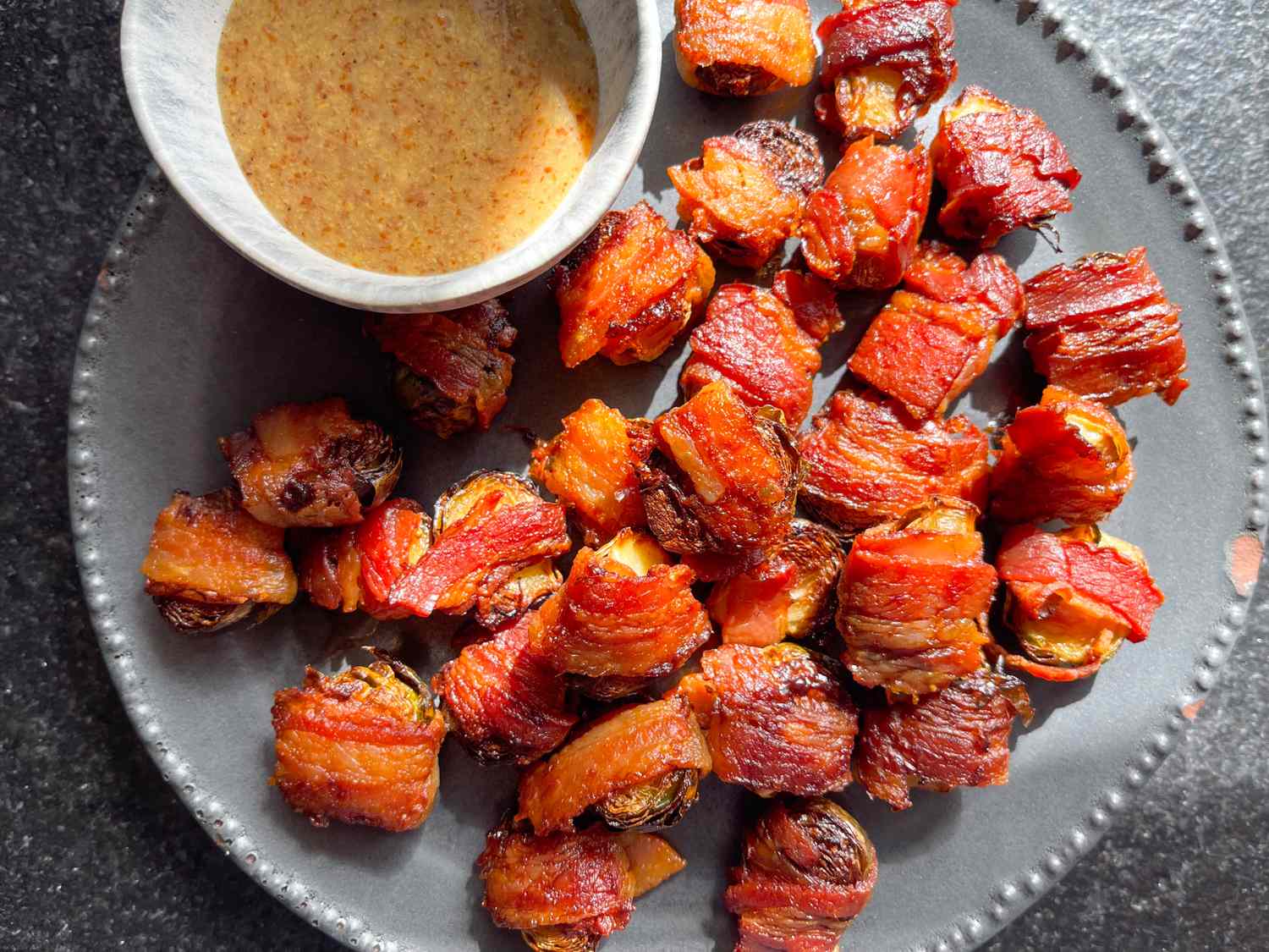 Baconwrapped Brussels sprouts on a plate with a small bowl of dipping sauce