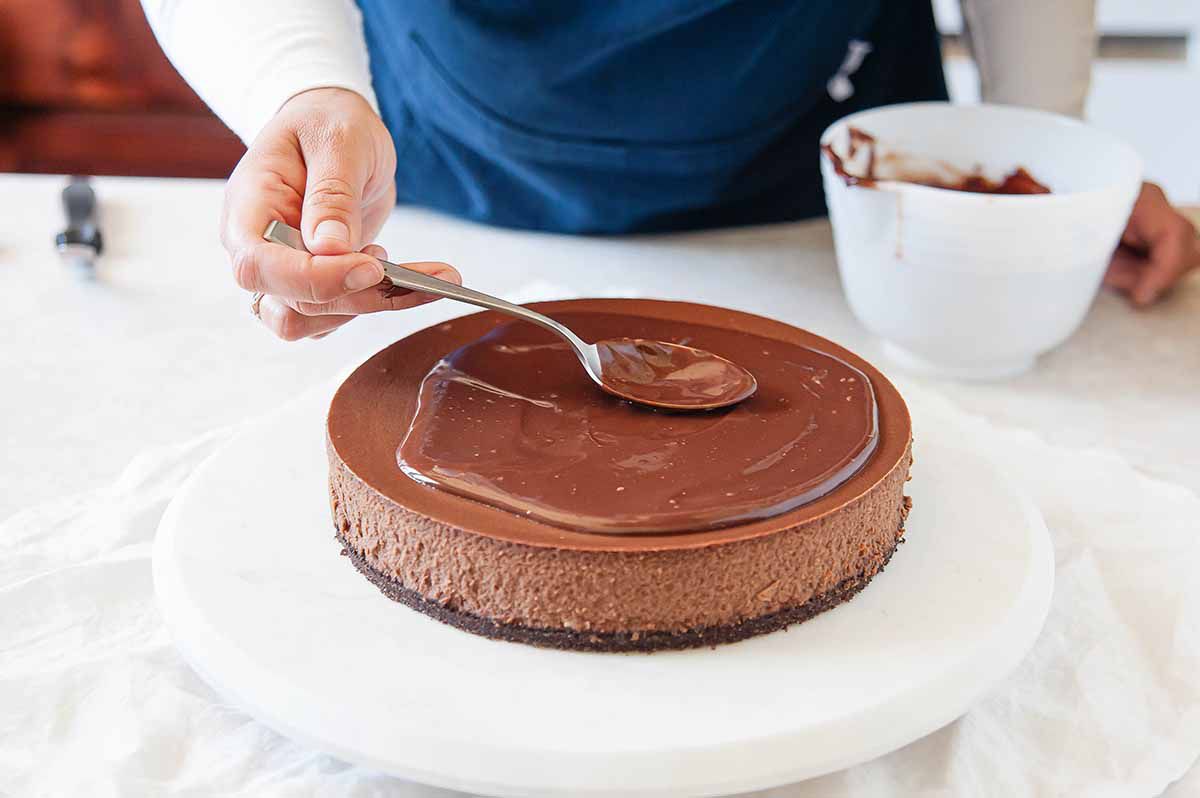 Using a spoon to smooth out the top of the ganache on chocolate cheesecake.