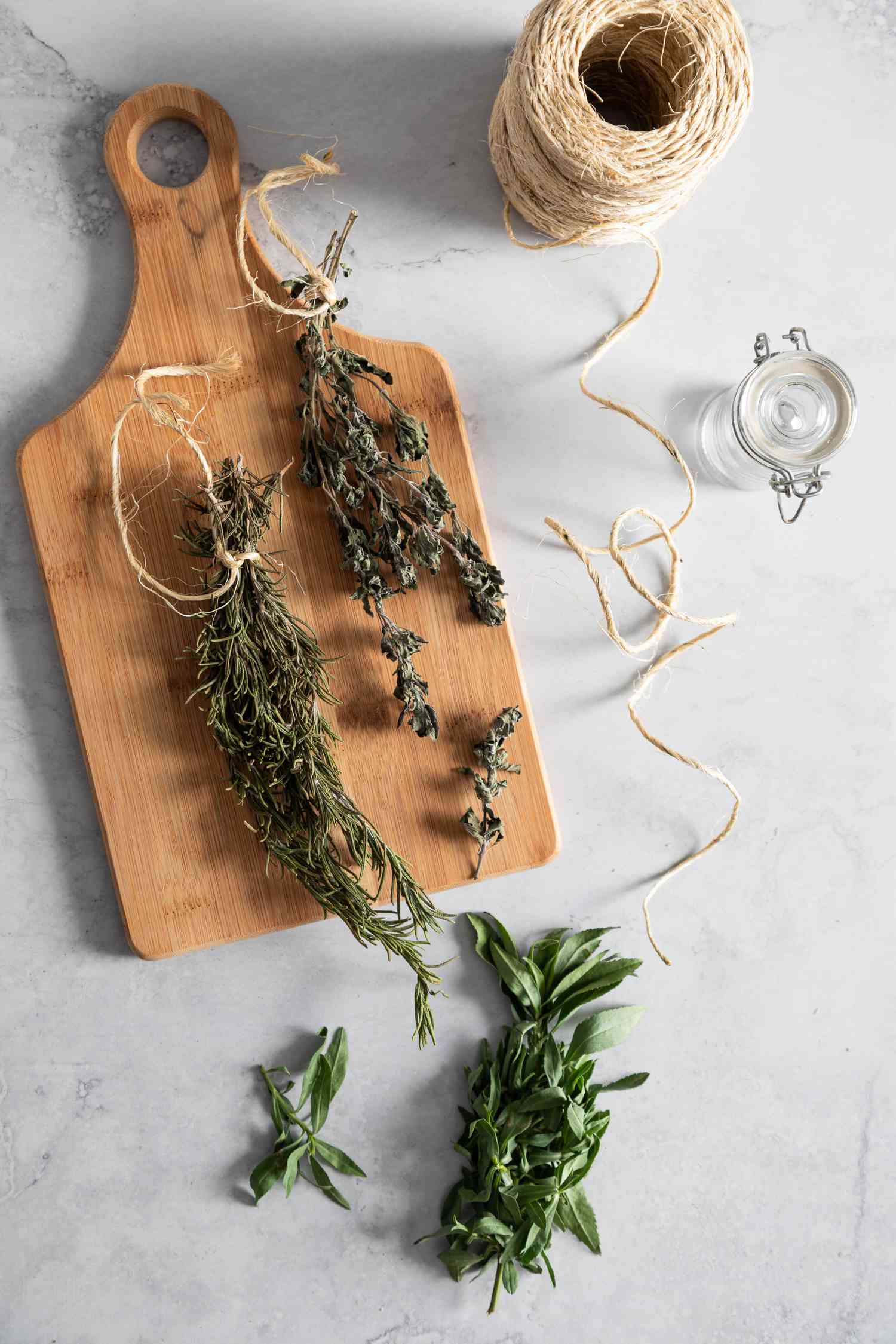 Sprigs of Dried Herbs on a Wooden Cutting Board Next to More Fresh Herbs and a Roll of Twine
