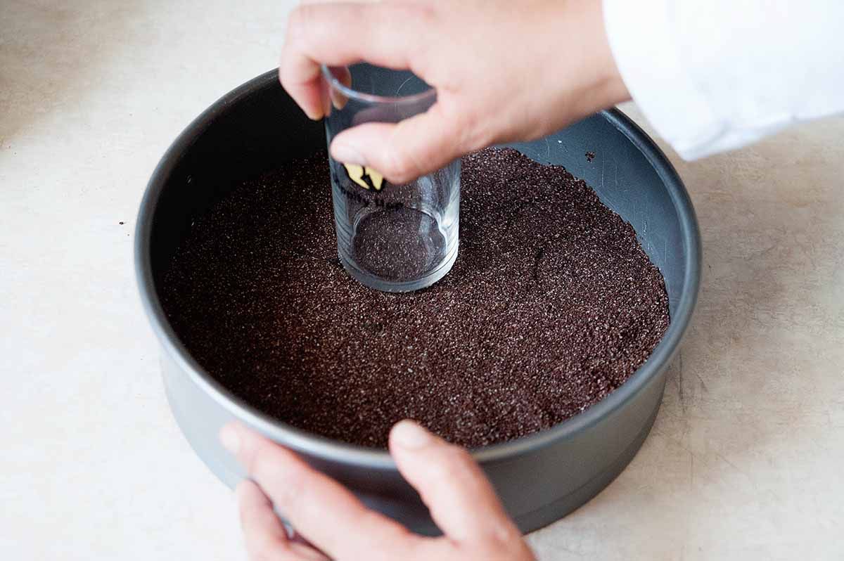 Chocolate graham crackers ground up and dumped into a spring form pan then pressed into an even layer with a cup to make the crust for a homemade chocolate cheesecake.
