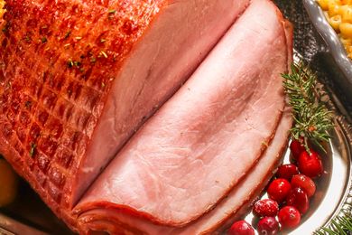 Sliced cooked ham served on a platter with garnishes like cranberries and herbs