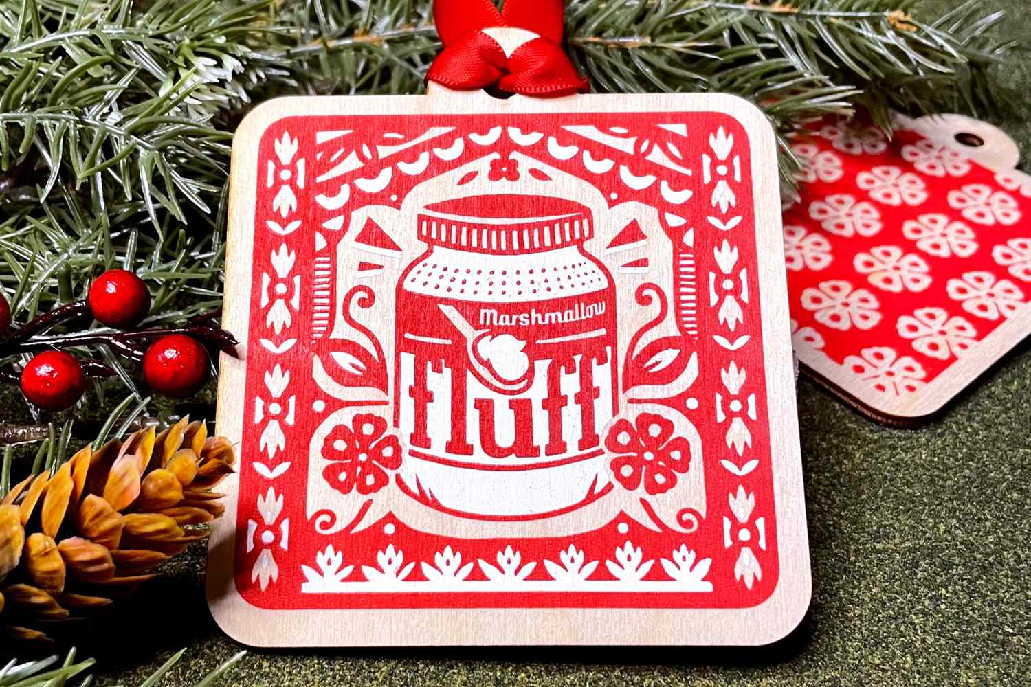 Marshmallow Fluffthemed ornament with decorative red and white design surrounded by pine and berries