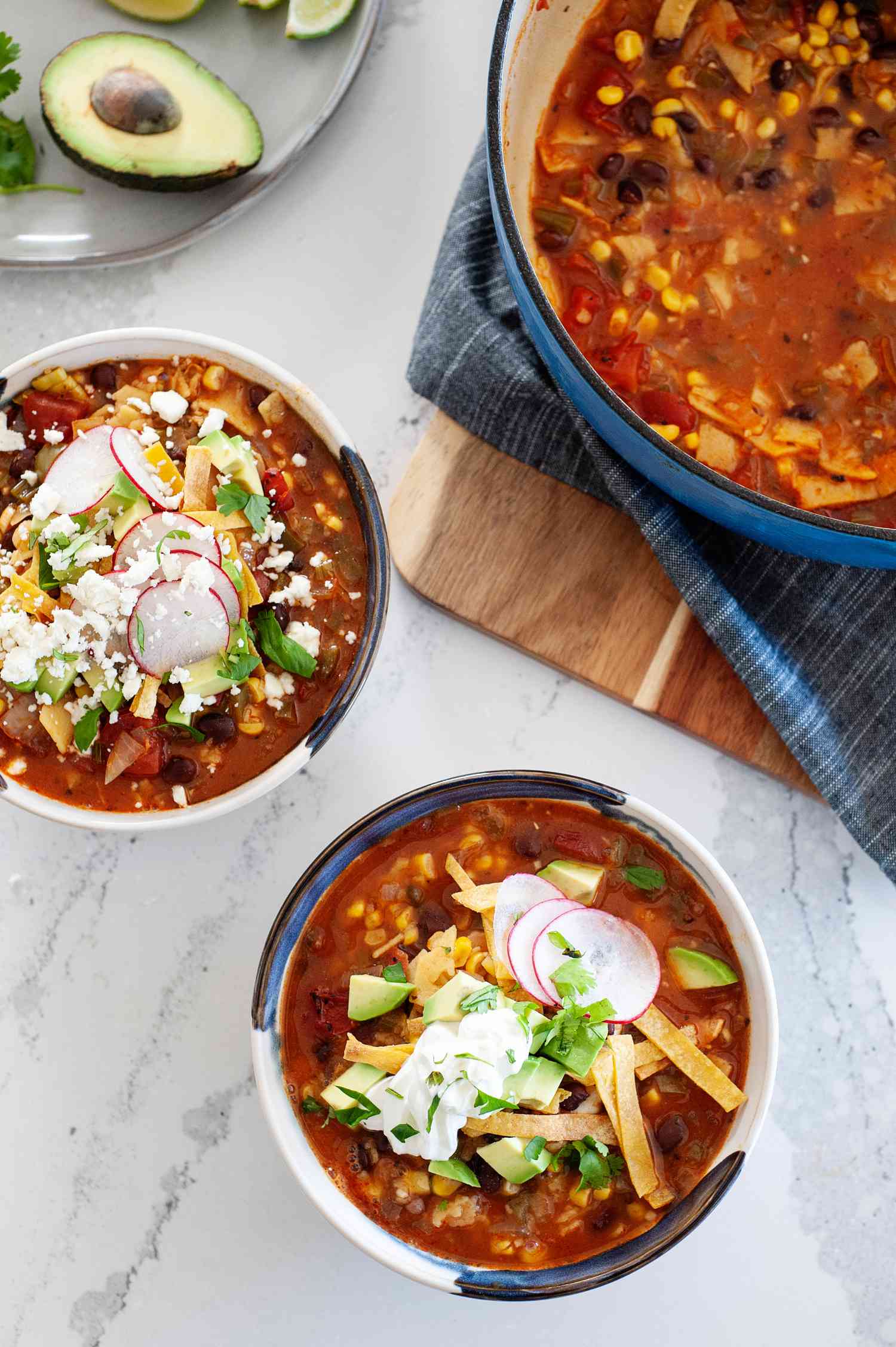 Meatless tortilla soup in a bowl topped with shredded cheese, sour cream, and tortilla strips.