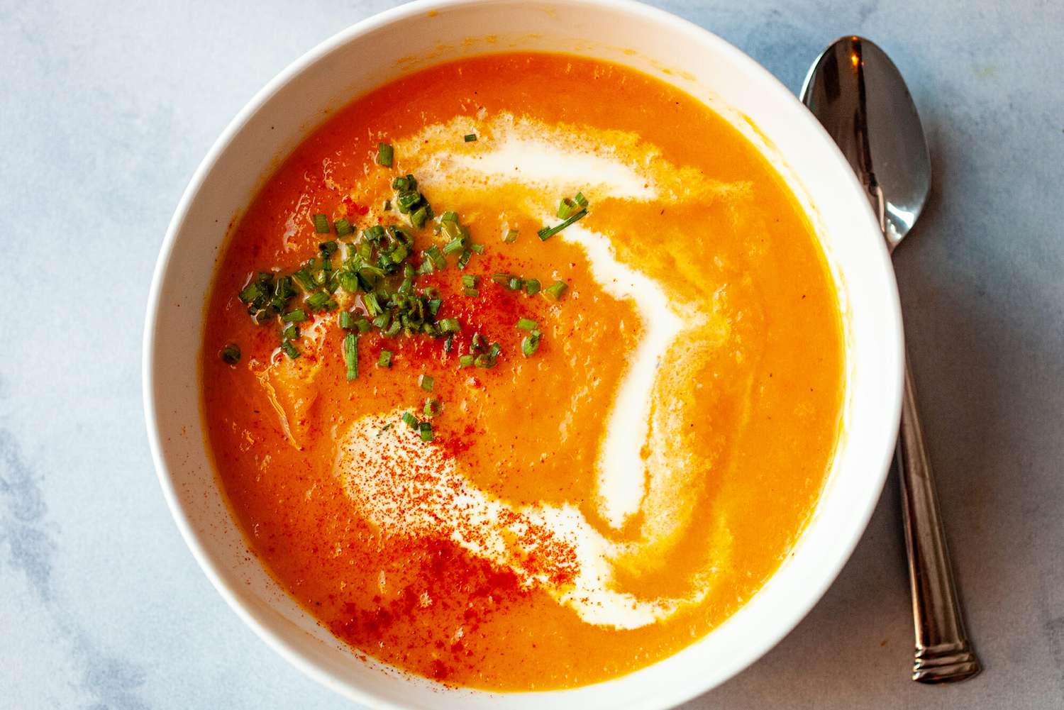 Overhead of a carrot soup topped with chives in a bowl with a spoon